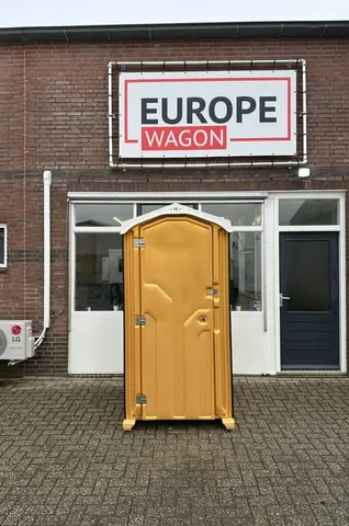 Een geel mobiel toilet dat voor een bedrijfsgebouw staat met een bord waarop ‘Europe Wagon’ staat