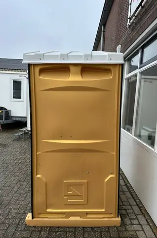 Een gele mobiele toiletcabine die buiten op een betegeld terrein staat