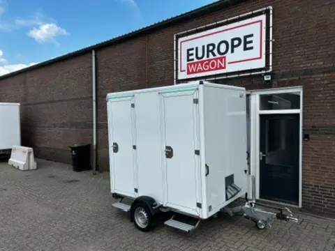 Twee mobiele toiletten naast elkaar met op de achtergrond een informatiebord en groen gras