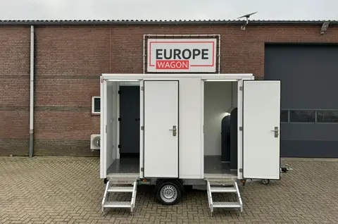Witte aanhangwagen met drie deuren geparkeerd voor een bakstenen gebouw ()