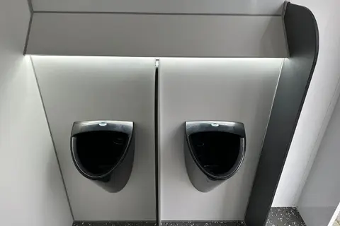 Twee donkere urinoirs tegen een grijze wand