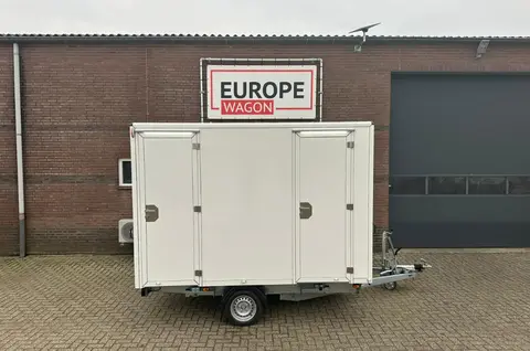 Witte aanhangwagen met drie deuren geparkeerd voor een bakstenen gebouw