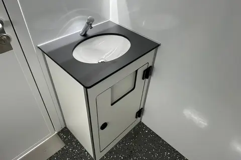 Wastafel in een compacte witte hoekruimte met zwart blad en ronde wasbak
