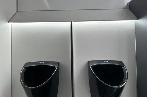 Een strak modern toiletgedeelte met twee donkere urinoirs en zachte verlichting