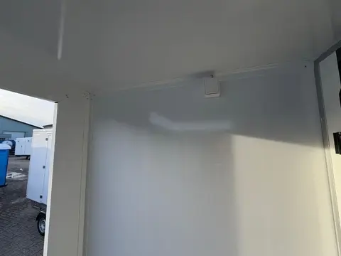 Binnenkant van een witte trailer met sanitaire voorzieningen; deur staat open waardoor het strakke hygiënische interieur zichtbaar is Model vacuum toiletwagen GL A van Europe Wagon