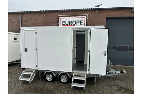 Witte aanhanger met twee open deuren en trapjes aan de voorkant geparkeerd op een bedrijventerrein