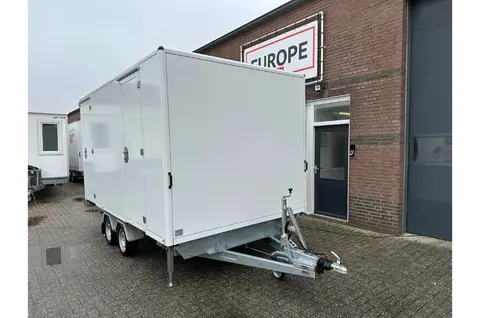 Witte aanhangwagen met dubbele deuren geparkeerd voor een bedrijfsgebouw