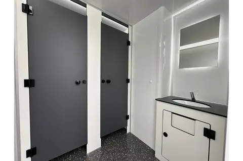 Een moderne sanitaire ruimte met twee afgesloten toiletcabines en een wastafel met spiegel