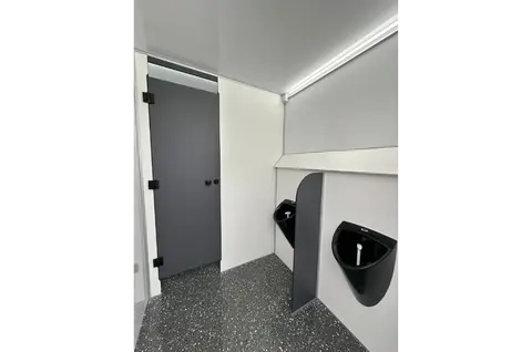 Een nette toiletruimte met twee urinoirs een privacybord en een gesloten deur op de achtergrond