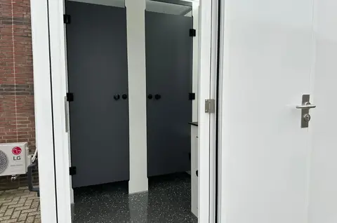 Ingang van een sanitaire ruimte met zicht op twee gesloten donkergrijze deurtjes en een glanzende zwarte vloer