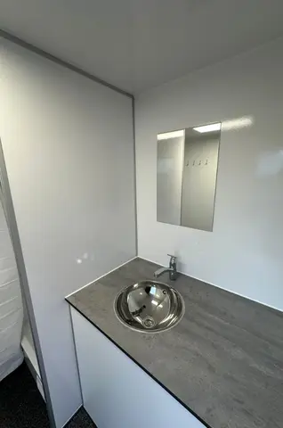 Wastafel met een ronde metalen wasbak en een kleine spiegel erboven in een strakke lichte ruimte