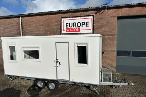 Een witte woonunit staat geparkeerd voor een bakstenen pand met het bord Europe Wagon