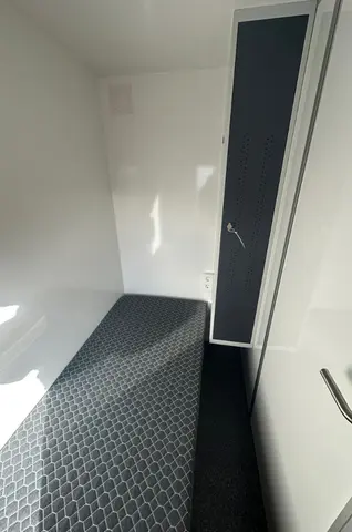 Kleine lichte ruimte met een smalle matras en een hoge kast ernaast